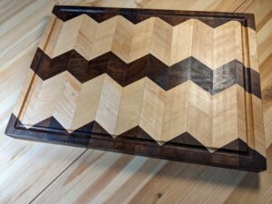 Walnut triangular shapes on edges on two sides and chevron down the middle of the board, maple chevrons in between in two strips, creating an appearance of hills and valleys on the flat cutting board.